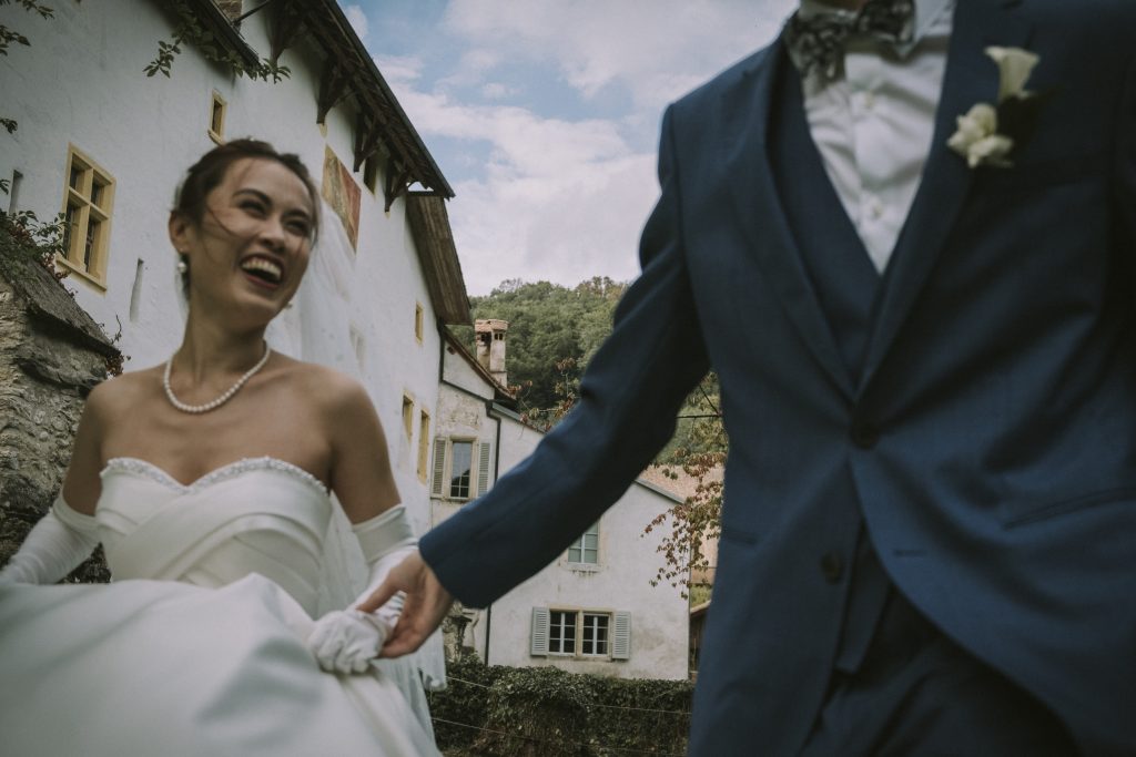 Un jeune couple de mariés cours main dans la main, dans le domaine de la maison du Prieur à Romainmôtier en Suisse.