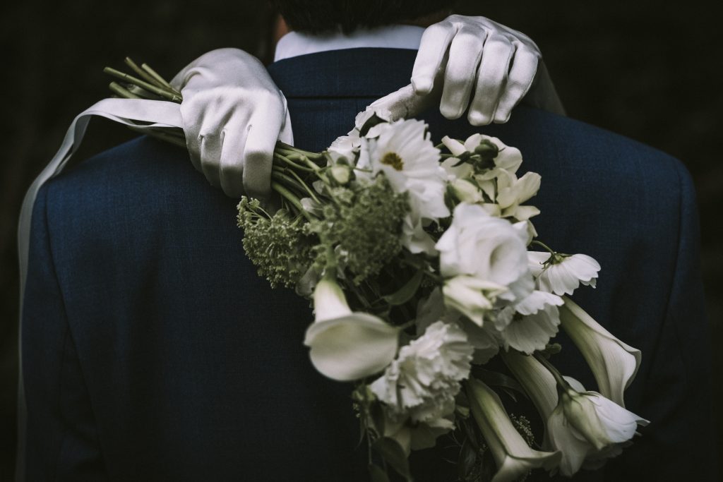 Un jeune couple vient de se marier dans le domaine de la maison du Prieur à Romainmôtier. On voit l'homme de dos, avec son costume. Et on voit le bouquet de la mariée et ses gants blancs.