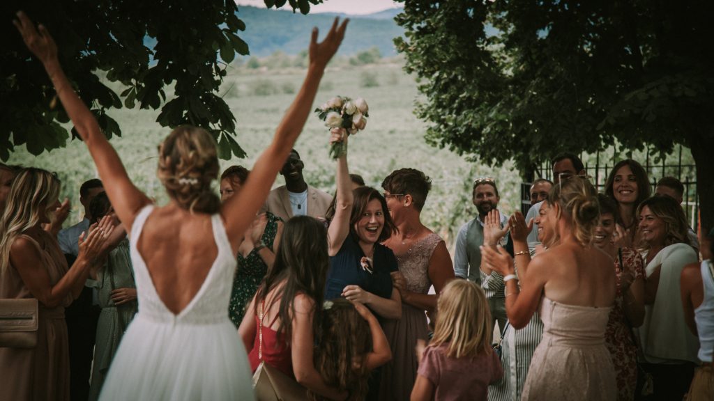 Le jour du mariage, la mariée lance son bouquet, une invitée le rattrape et tout le monde sourit et est joyeux.