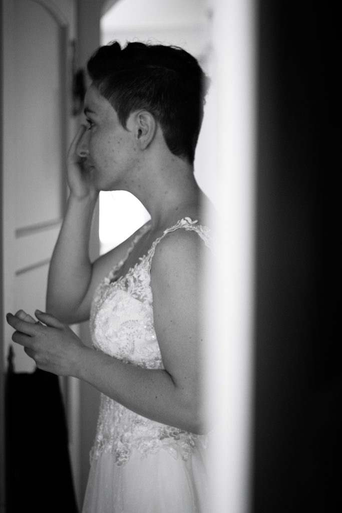 Une jeune femme, future mariée, se maquille avant la cérémonie. C'est les préparatifs. On voit sa robe de mariée.
