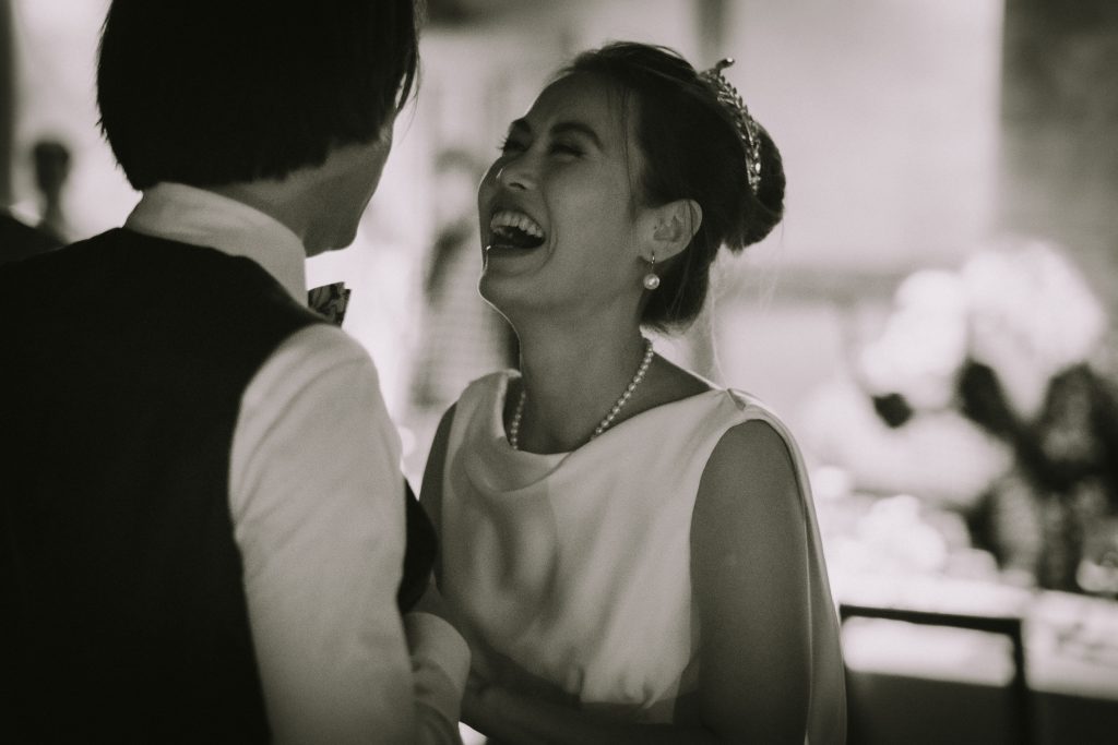 Un jeune couple de mariés dansent le soir de leur mariage. La femme rit. On voit la robe de mariée, sa coiffure et ses bijoux.
Je suis photographe de mariage basé en Suisse.