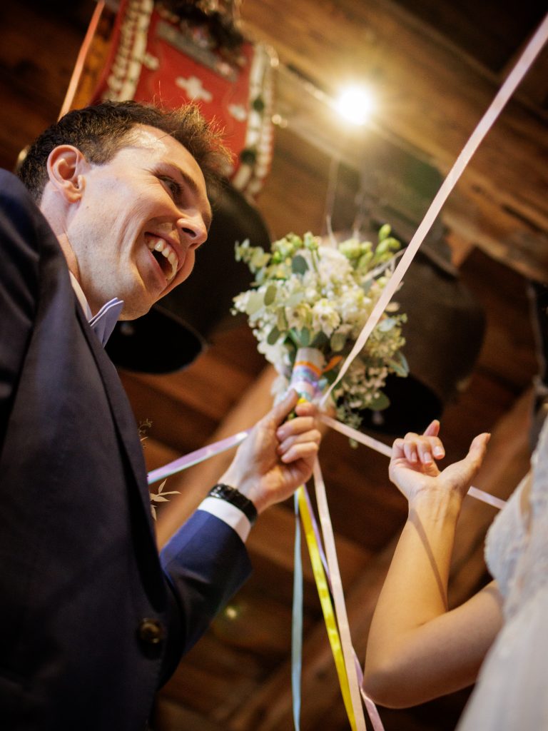 C'est le lancer de bouquet lors d'un mariage à Champoussin dans le restaurant chez Gaby. Le marié tient le bouquet autour duquel des liens de couleur sont attachés. Il rit .