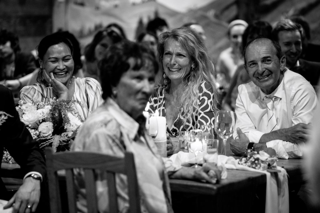 Les parents des mariés rient lors d'un discours pendant le repas de mariage. La photo est en noir et blanc. La mère de la mariée est très émue.