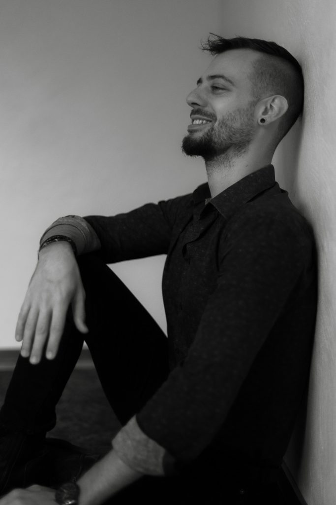 Photo de moi, Clément Lambla, en noir et blanc. Je suis assis et je souris.